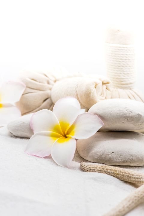 Ruhiges Spa-Detail: weiße Kerze und Frangipani auf hellem Sand